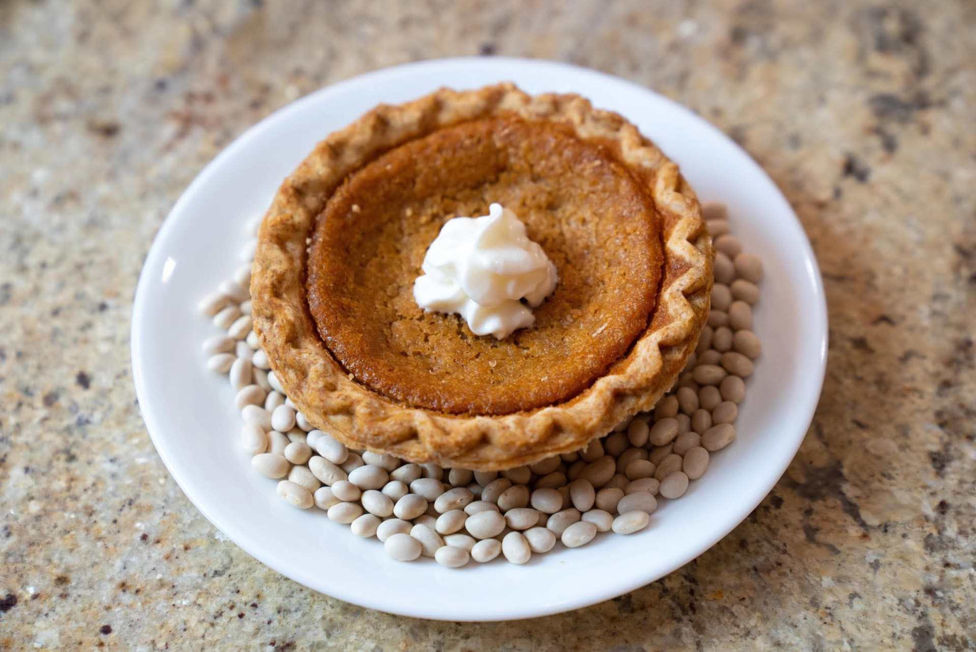 A freshly baked Supreme Bean Pie topped with whipped cream, served on a bed of navy beans