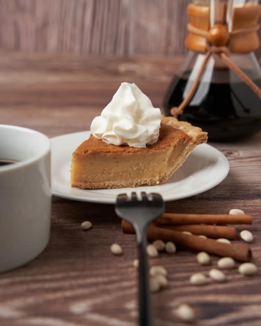A slice of Supreme Bean Pie topped with whipped cream, served with coffee